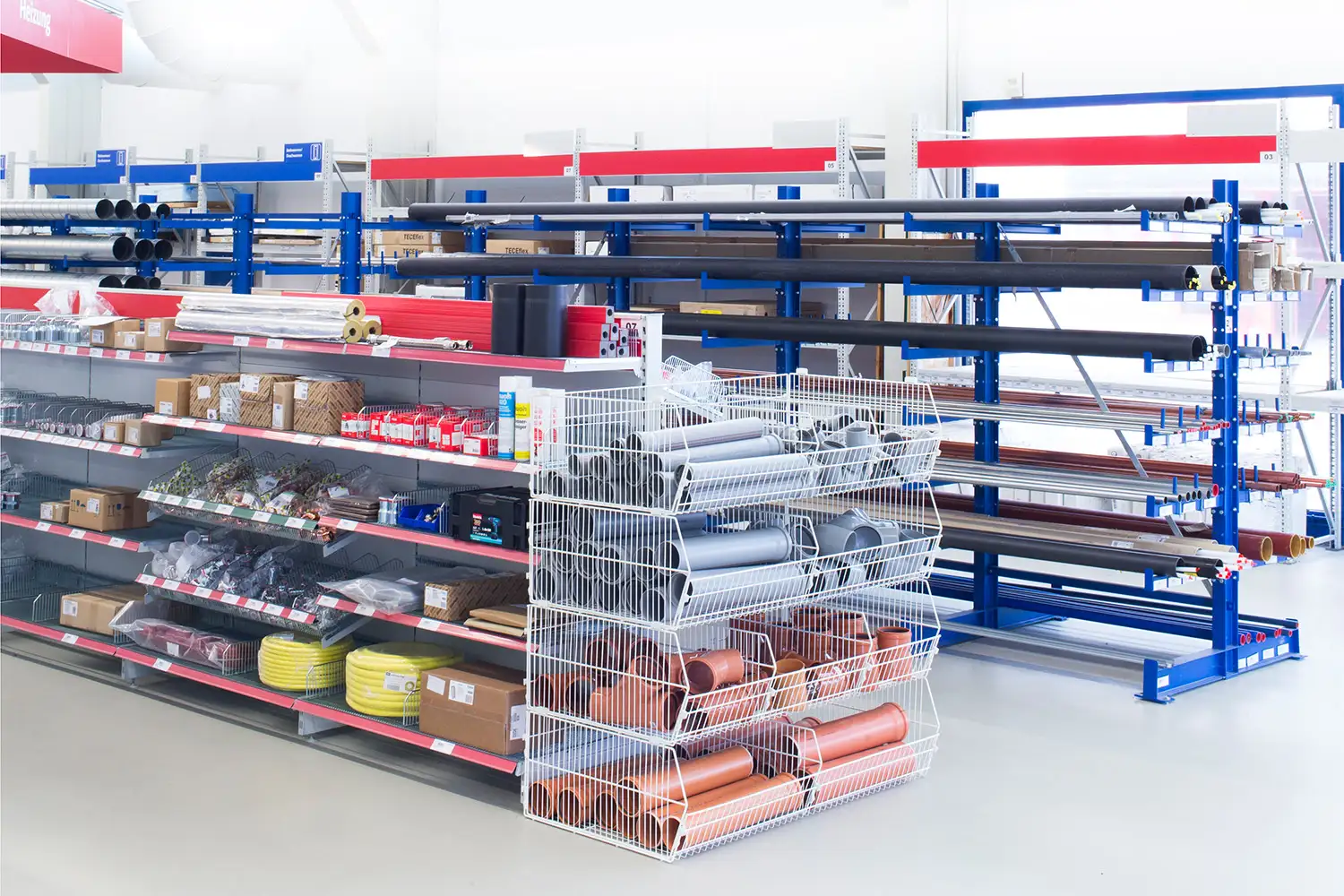 Verkaufsfläche in einem Baumarkt mit Regalen voller Sanitärartikel, Rohre, Dichtungen und Zubehör, übersichtlich in Drahtkörben und auf Fachböden präsentiert.