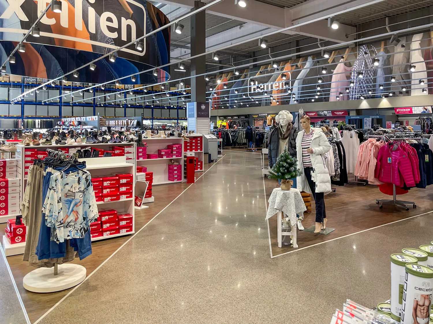 Moderne Textilabteilung in einem Einzelhandelsgeschäft mit klar strukturierter Herrenmode, gut sichtbarer Beschilderung und ansprechender Produktpräsentation für ein angenehmes Einkaufserlebnis.