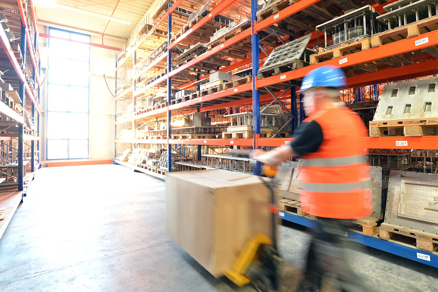 Großes Lager mit Hochregalen und einem Mitarbeiter beim Transport von Waren. Optimales Beispiel für Lagerlogistik, Regalprüfung und innerbetriebliche Prozesse.