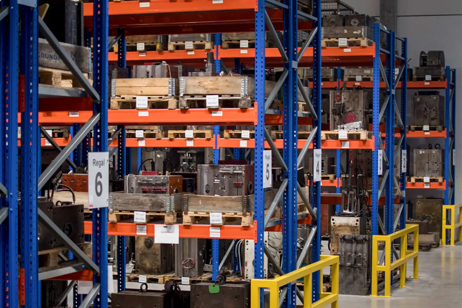 Ein ähnlicher Blick auf Schwerlastregale mit nummerierten Bereichen (z. B. Regal 4 bis 6); die Regale enthalten zahlreiche große Metallteile auf Paletten, das Lager ist sauber und strukturiert.