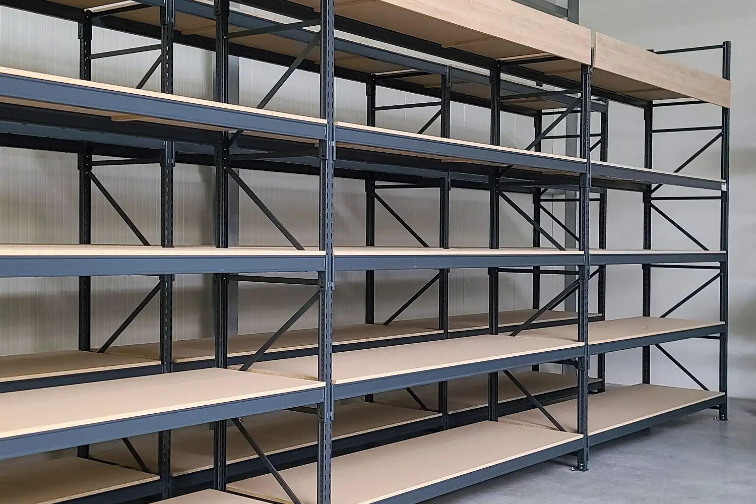 Leere Lagerregale mit schwarzem Metallrahmen und Holz-Einlegeböden, aufgestellt in einem hellen, sauberen Raum mit glattem Boden.