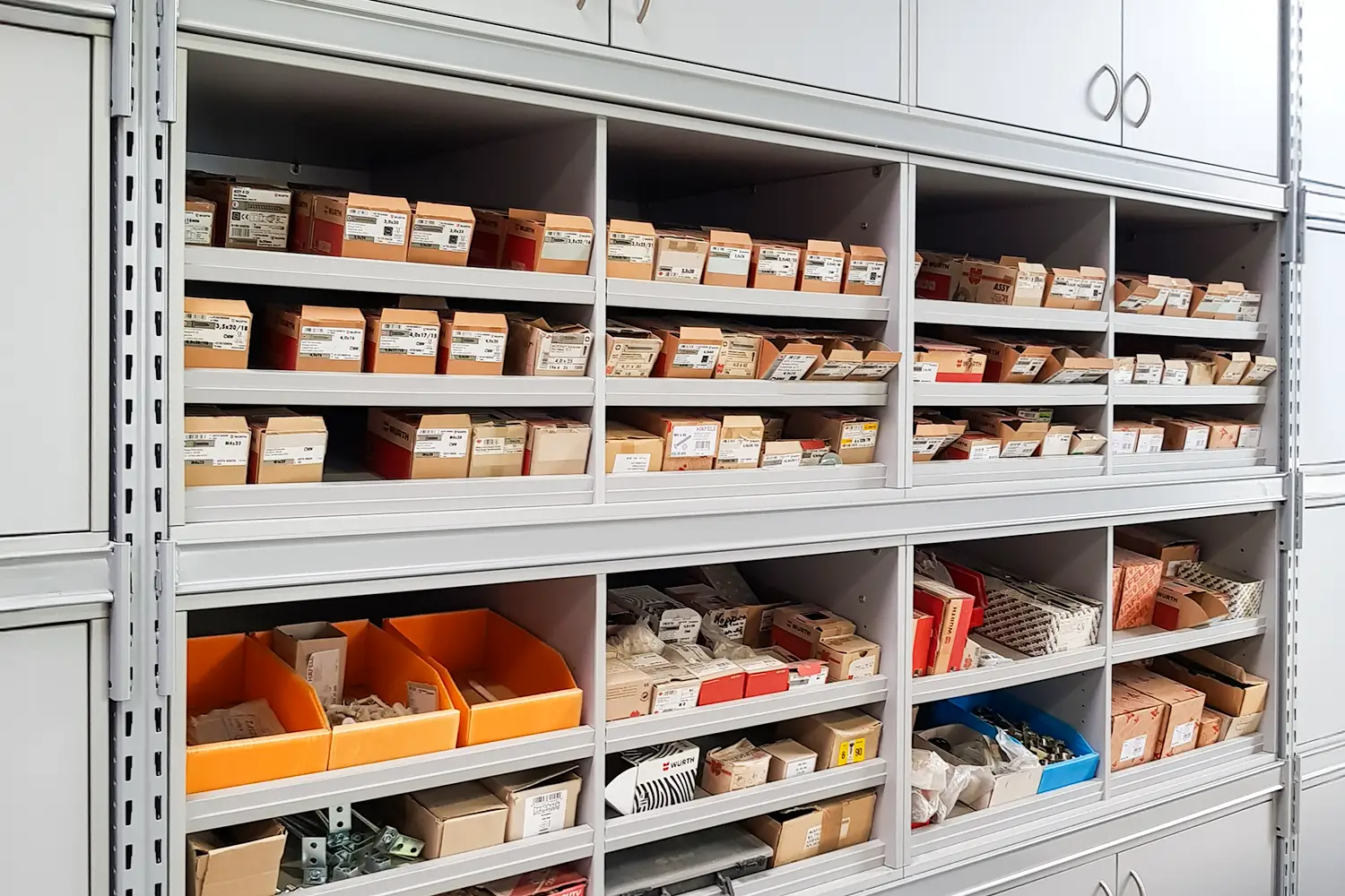 Metallregalsystem mit vielen kleinen Boxen, gefüllt mit Ersatzteilen und Zubehör; die Teile sind beschriftet und farblich sortiert in Fächern gelagert.