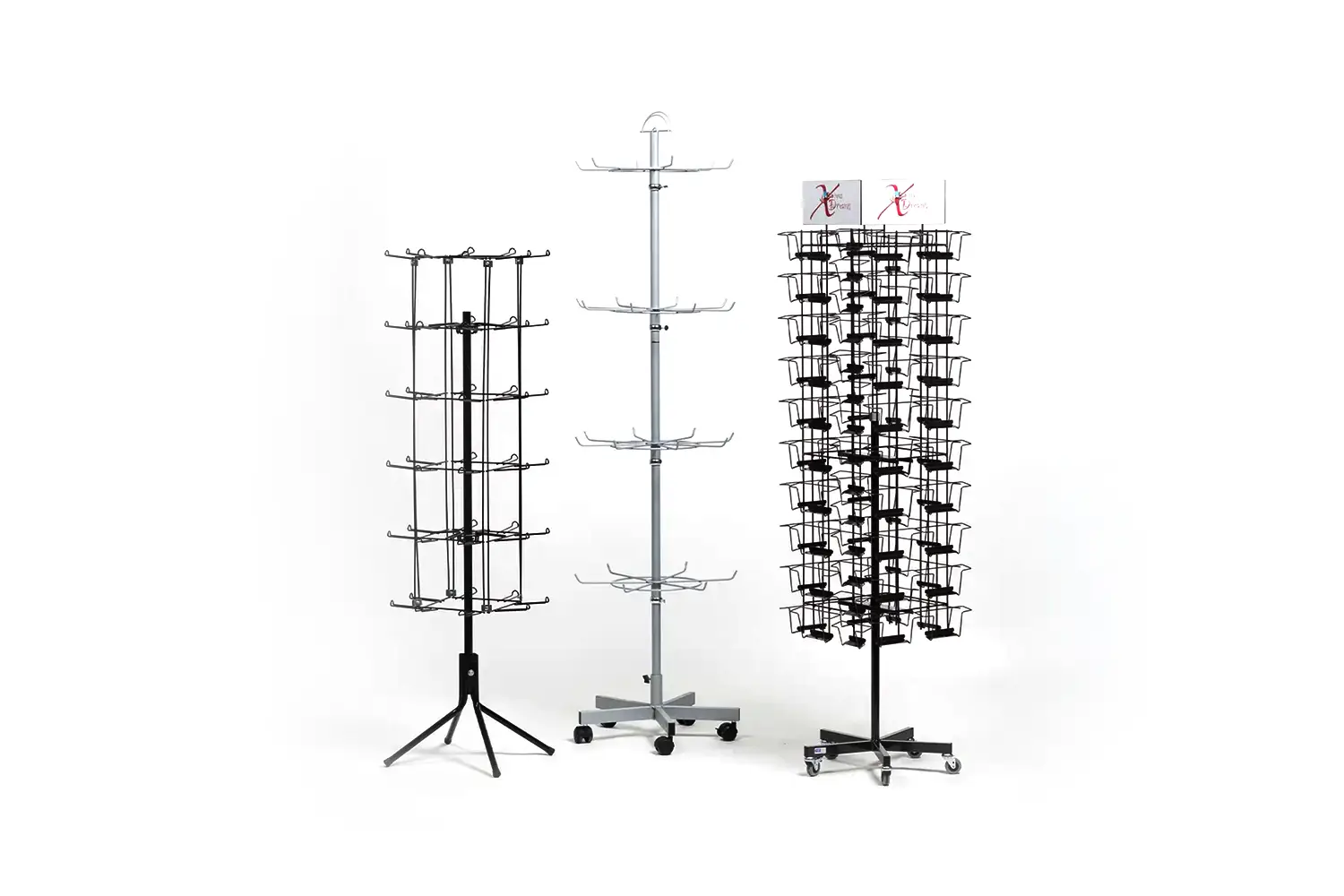 Drei verschiedene drehbare Verkaufsständer auf Rollen, jeweils mit Metallhaken oder Drahtkörben, für Produkte wie Zubehör oder Karten.