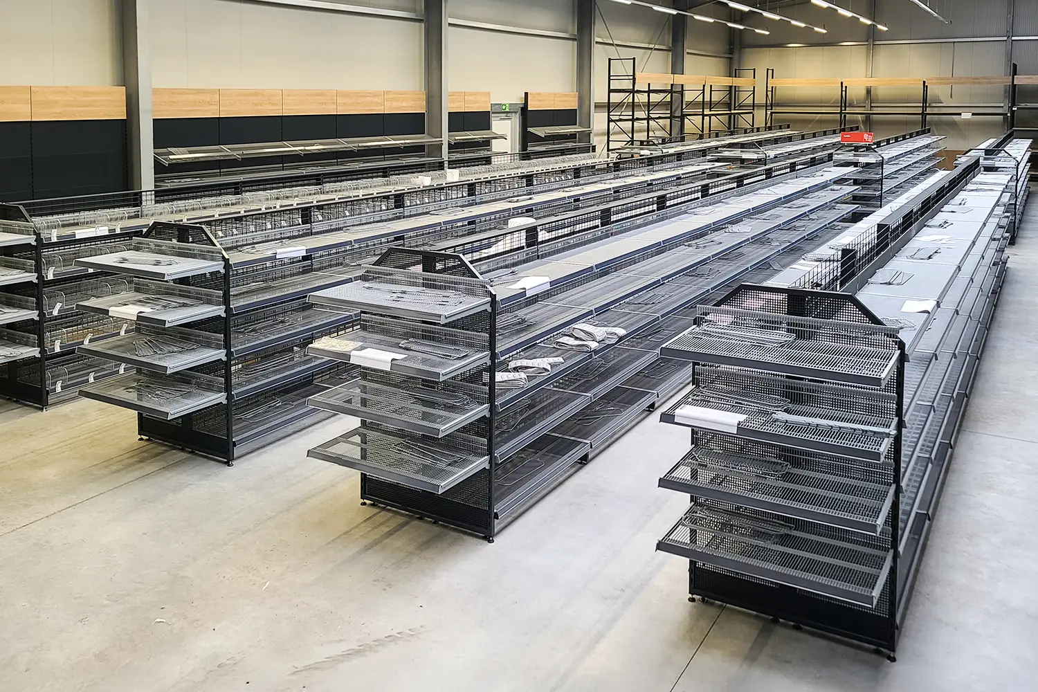 Großes Lager oder Fachmarkt mit zahlreichen langen, leeren Regalen aus Metall und Gitterkörben, geeignet für die Warenpräsentation.