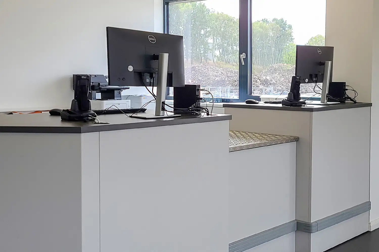 Zwei moderne Kassenarbeitsplätze mit Monitoren und Scannern in einem hellen Raum mit Fenster und schlichter Einrichtung.