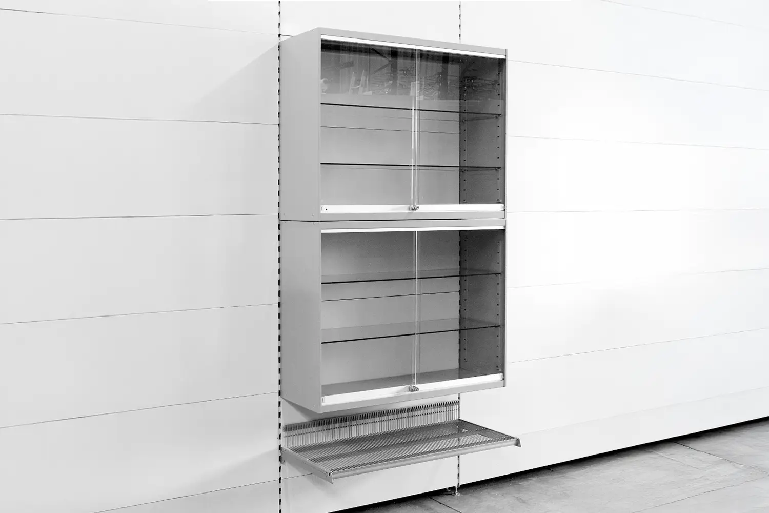 Eine an der Wand montierte Vitrine mit zwei verglasten Fächern und einem Drahtgitterboden. Sie dient zur Präsentation von Waren.